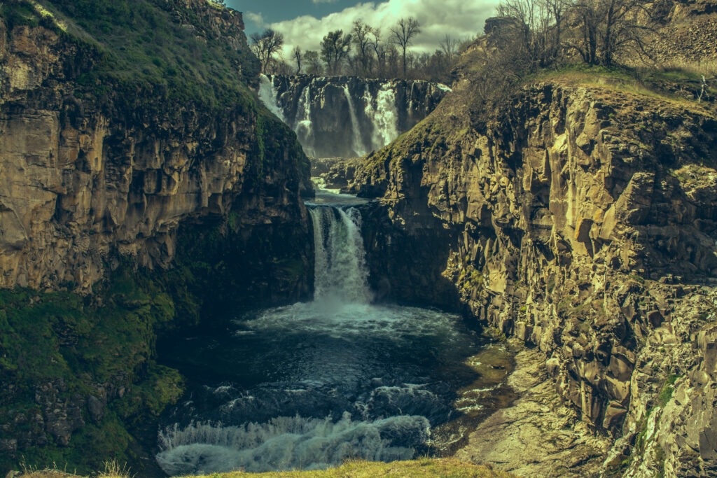 Majestic waterfall cascading over rugged cliffs with rocky stones in earthy tones wallpaper background