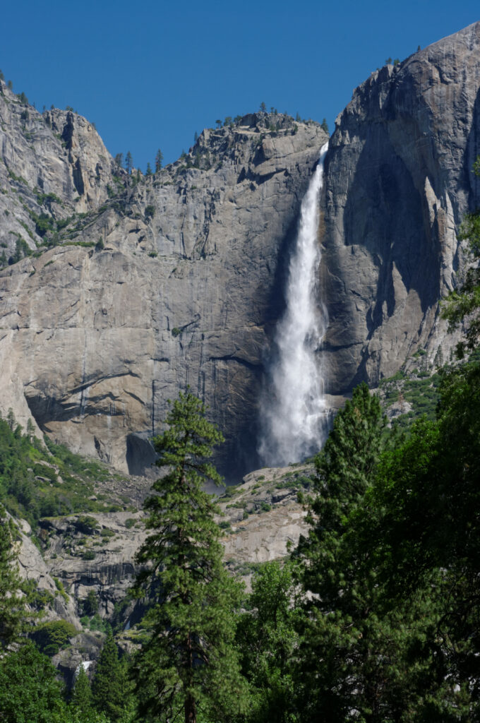 Majestic waterfall cascading down rocky cliffs with lush green trees and clear blue sky backdrop Wallpaper