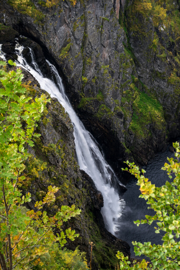 Powerful waterfall cascading down rugged cliffs surrounded by vibrant green trees nature wallpaper