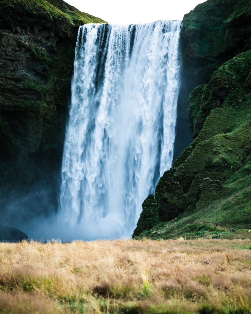 Majestic waterfall cascading over rugged cliffs with lush green moss and sunlight highlights Wallpaper