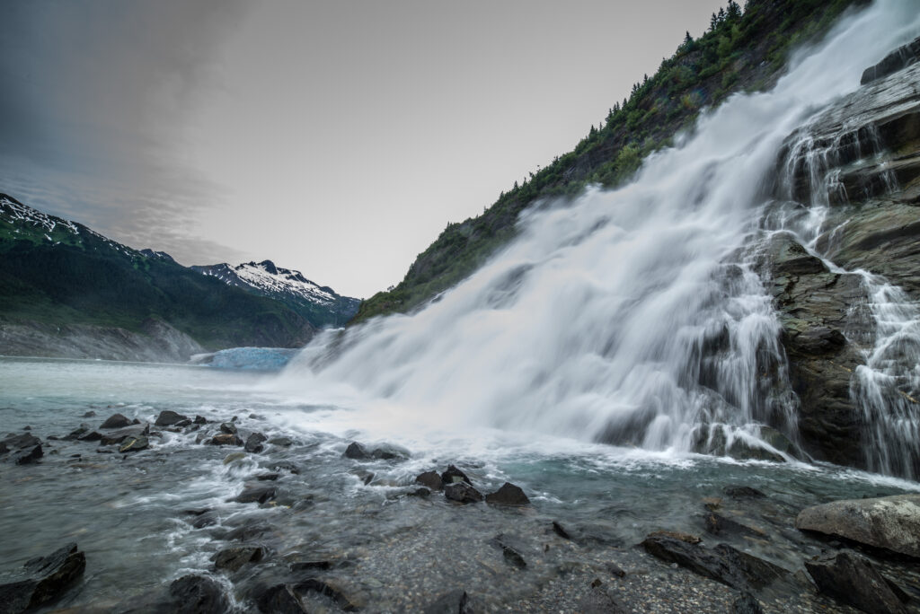 Majestic waterfall cascading over rocky stones with misty mountains in blue grey tones wallpaper