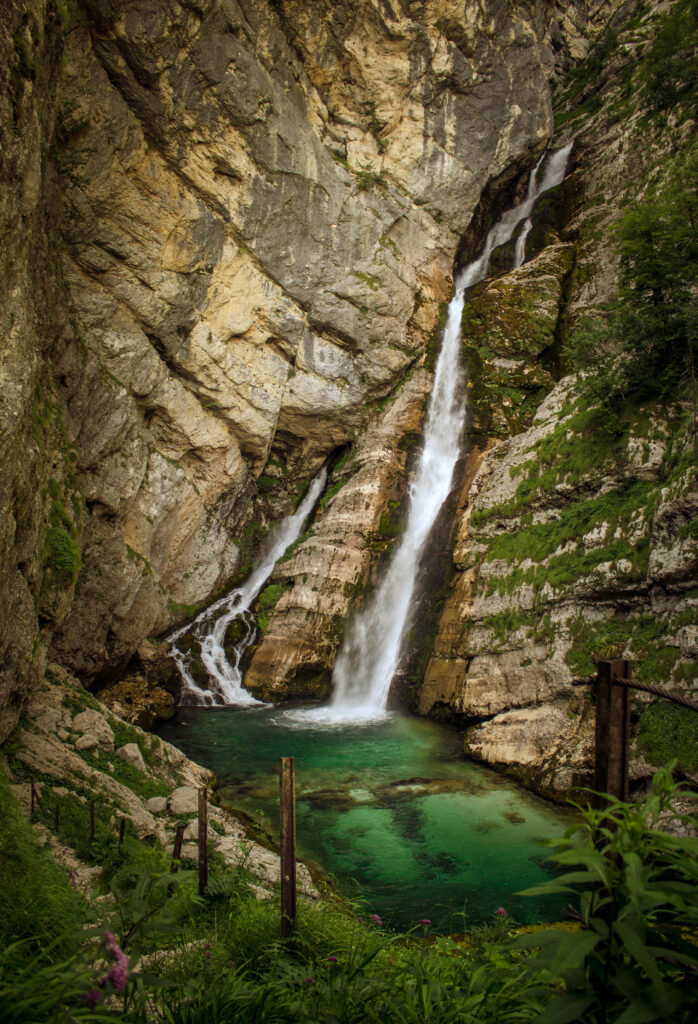 Majestic waterfall cascading into emerald pool surrounded by lush grass and steep cliffs wallpaper