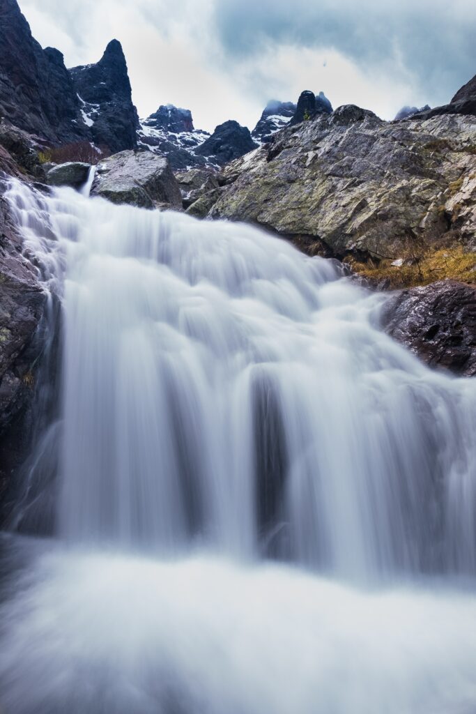 Waterfall cascading over smooth rocks with mountains and cloudy sky in serene natural landscape Wallpaper