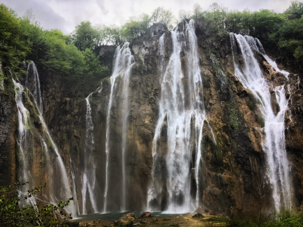 Majestic waterfall cascading over rocky cliffs surrounded by lush green foliage wallpaper background