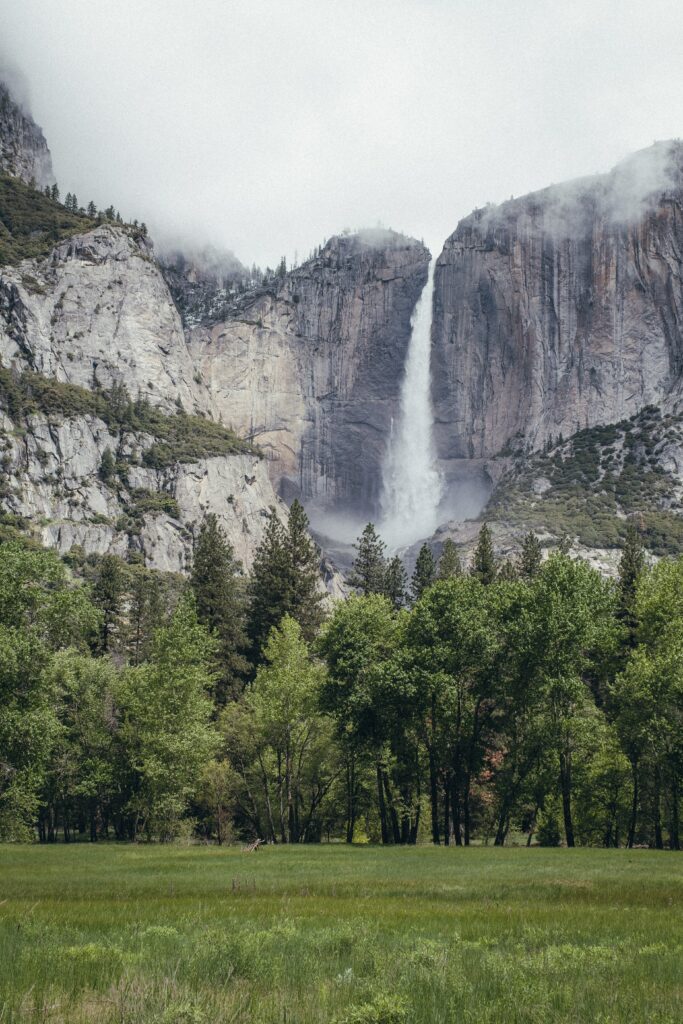 Majestic waterfall cascading over rugged rocks with lush green trees and mountain backdrop wallpaper