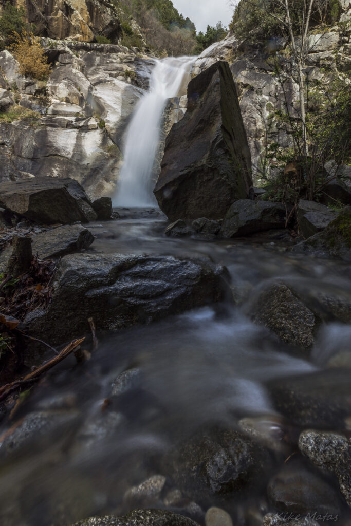 Majestic waterfall cascading over rugged rocks surrounded by lush green forest in serene landscape Wallpaper