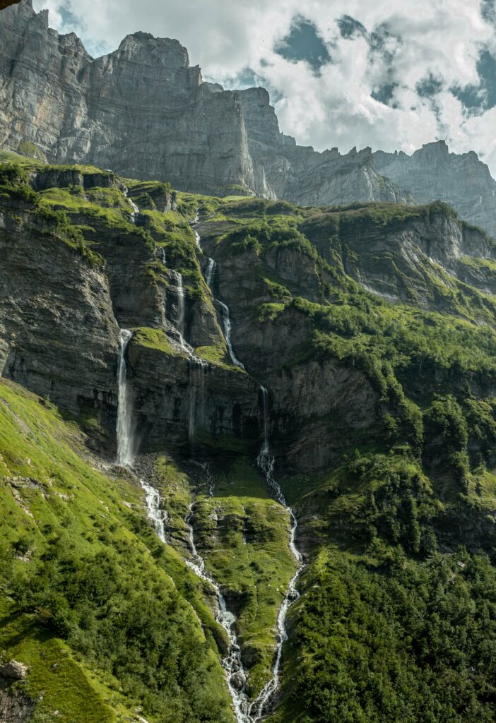 Majestic waterfall cascading rocky cliffs surrounded by lush green forest under cloudy sky wallpaper