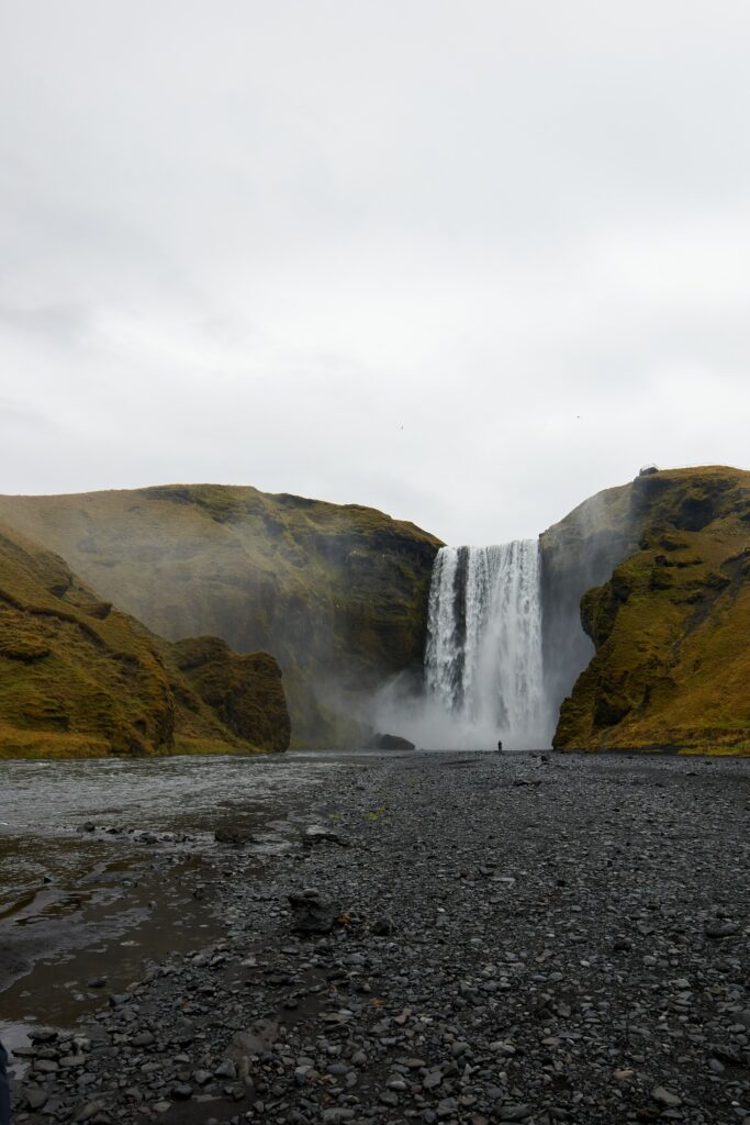 Majestic waterfall cascading over mossy cliffs and rugged rocks with pebbles in foreground Wallpaper