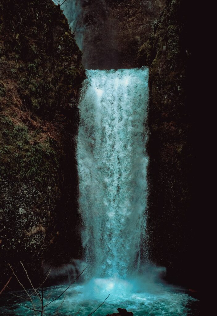 Powerful waterfall cascading over rugged cliff with mossy rocks and vibrant blue water background Wallpaper