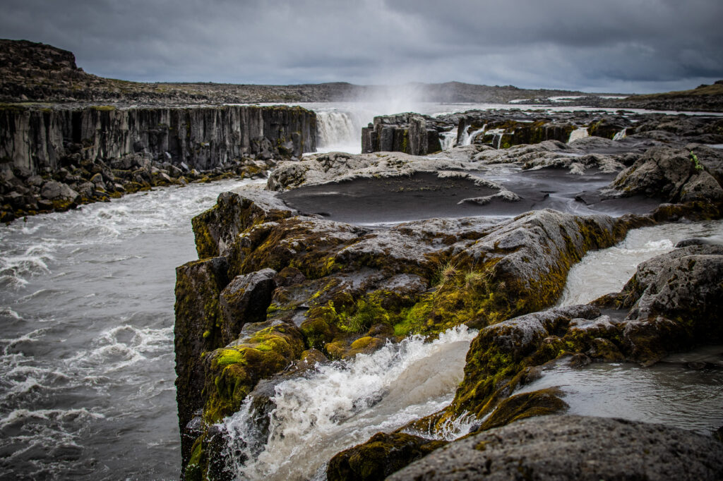 Powerful waterfall over rugged cliffs with lush moss under moody overcast sky wallpaper background
