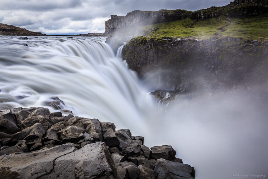 Majestic waterfall cascading over rugged cliffs with mist mountains and lush green forest background Wallpaper