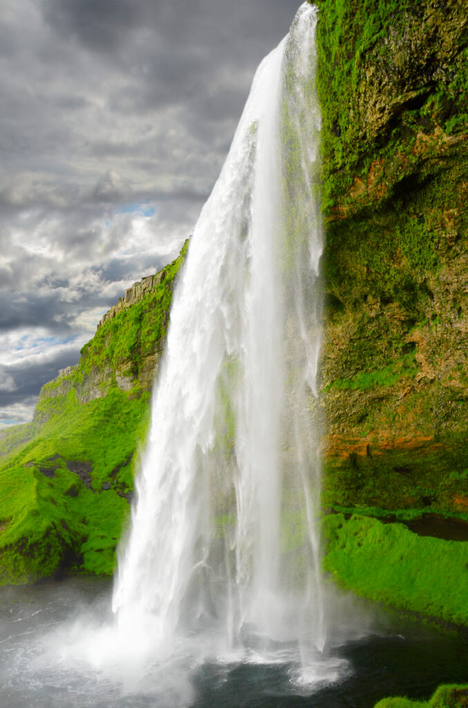 Majestic waterfall cascading over mossy rocks under dramatic cloudy sky natural landscape wallpaper