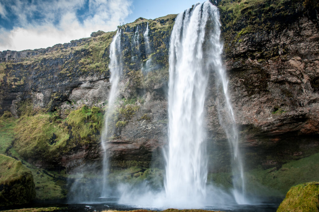 Powerful waterfall cascading over rocky cliffs with lush green moss under bright sky wallpaper