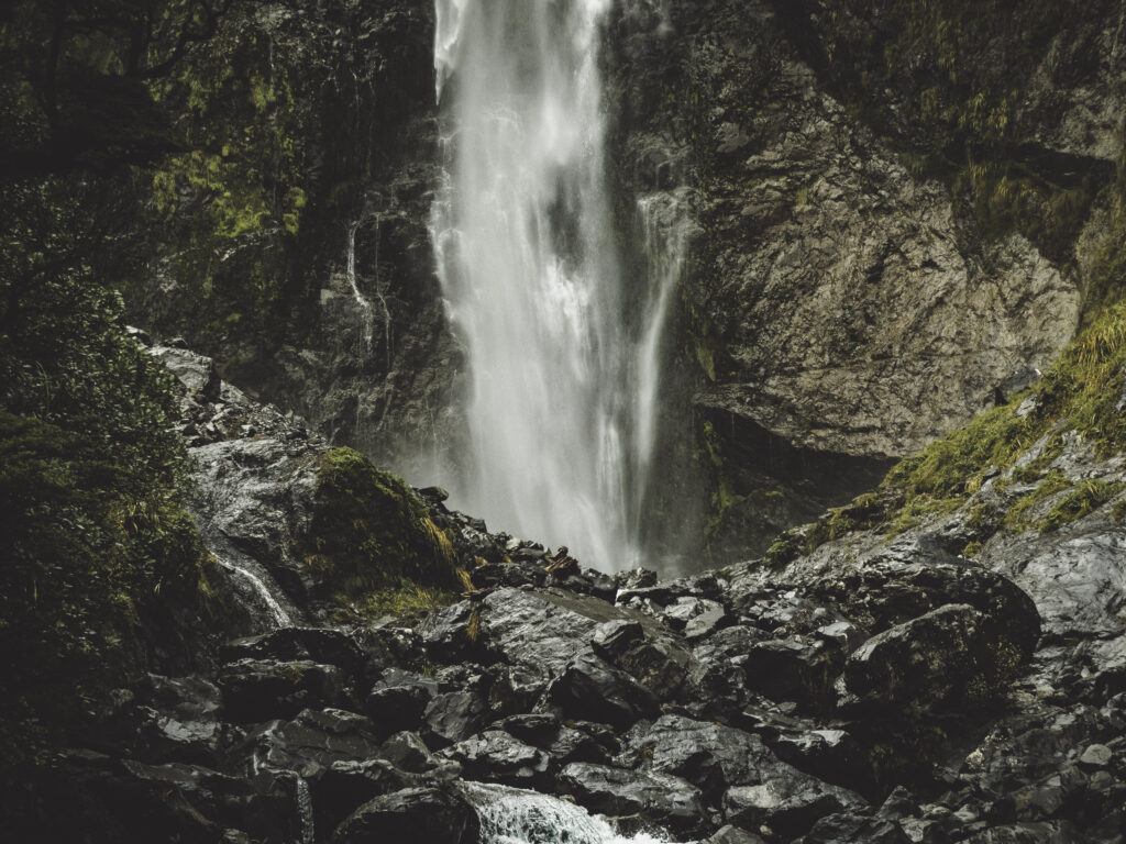 Waterfall cascading over rugged stones with lush green foliage creating a tranquil scene Wallpaper