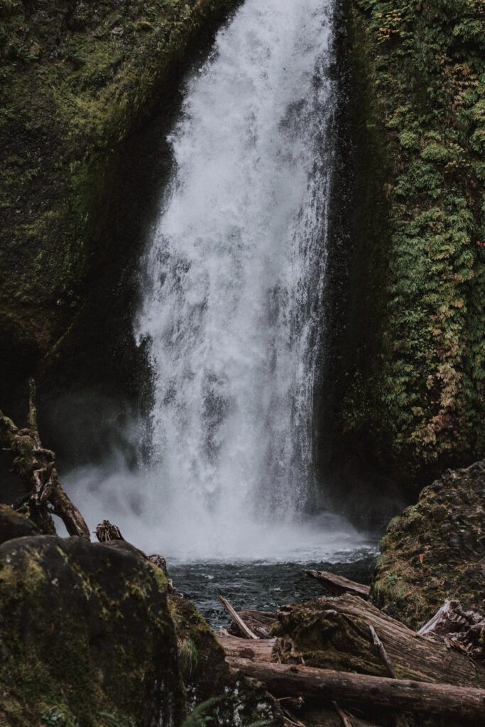 Majestic waterfall cascading over rugged rocks surrounded by lush greenery and misty spray Wallpaper