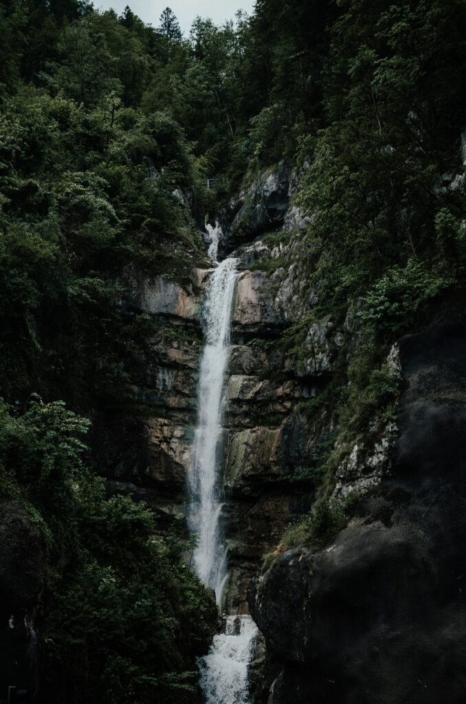 Majestic waterfall cascading down rugged cliff surrounded by dense lush green forest wallpaper