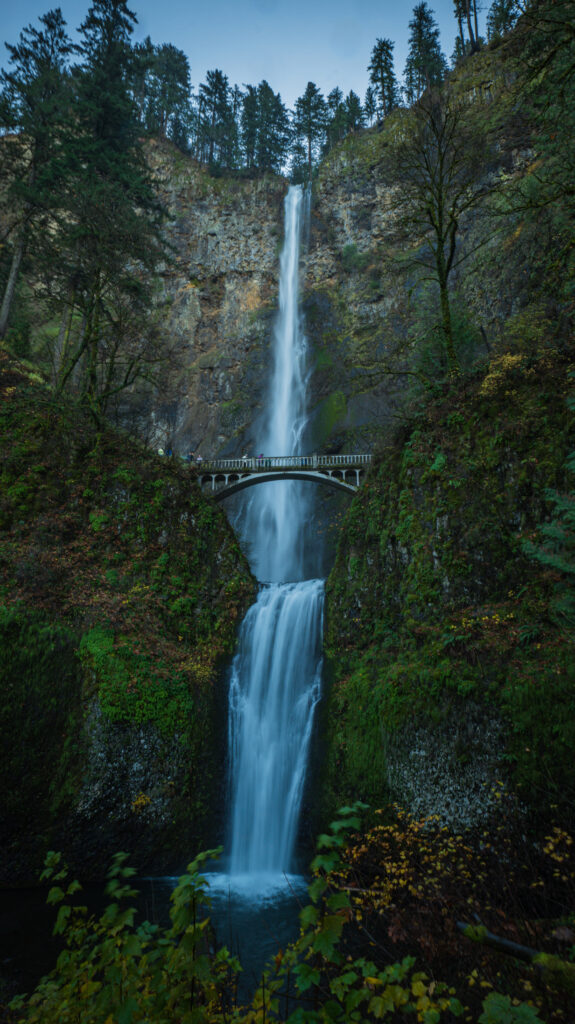 Majestic waterfall cascading over rocky cliffs with lush greenery and a charming wooden bridge Wallpaper