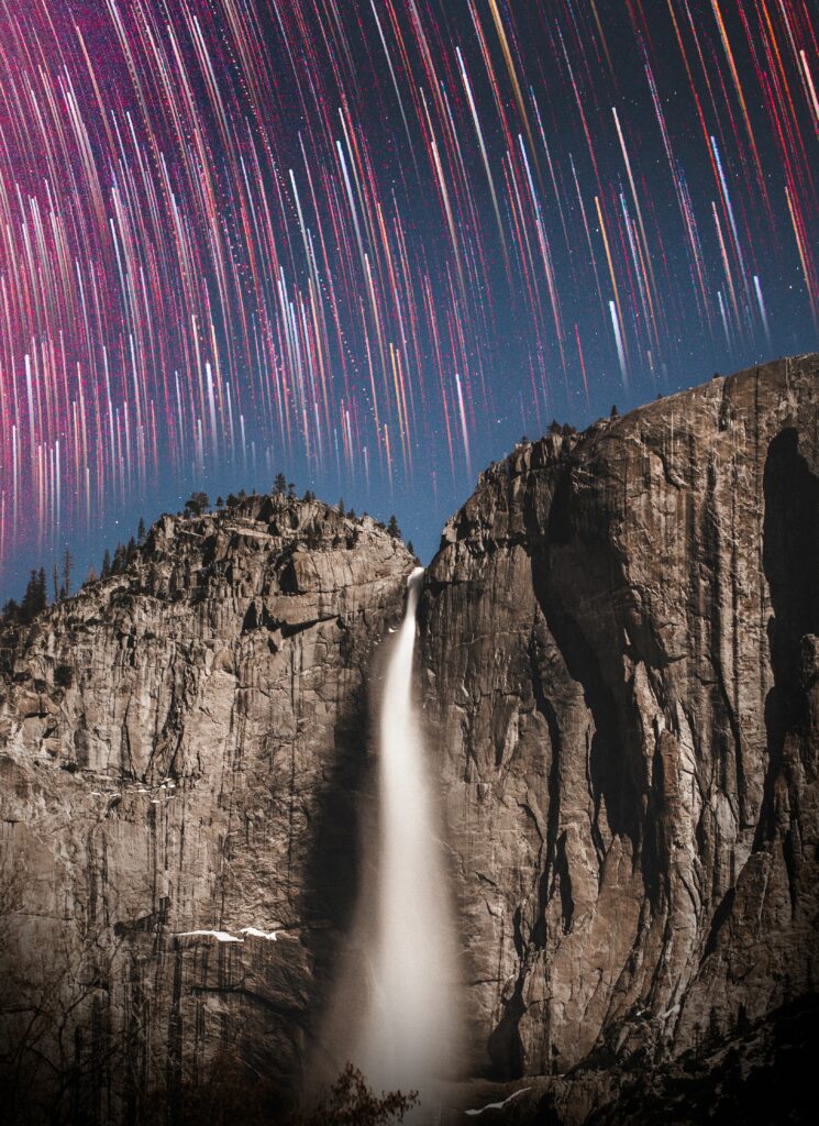 Majestic waterfall over rugged cliffs beneath vibrant star trails in a tranquil night sky wallpaper
