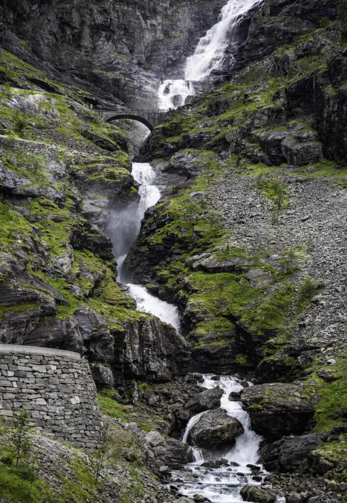 Cascading waterfall over rocky cliffs with stone bridge and lush greenery mountain landscape wallpaper