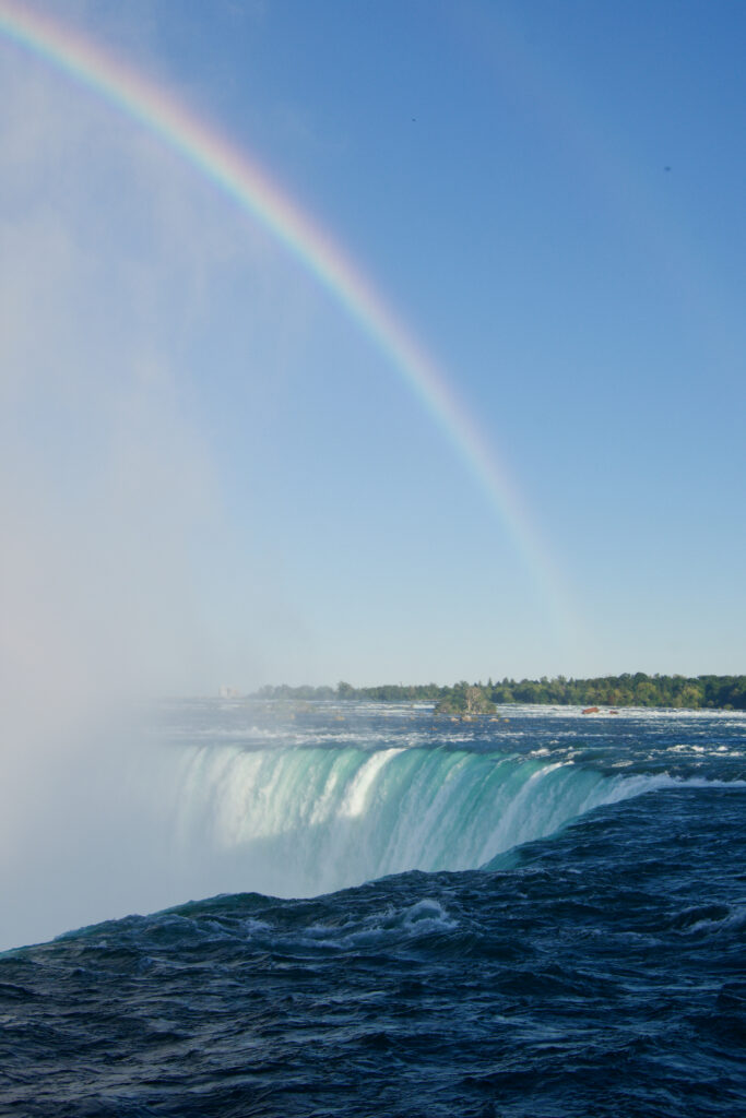 Majestic waterfall cascading over rugged stone with mist and vivid rainbow in clear blue sky Wallpaper