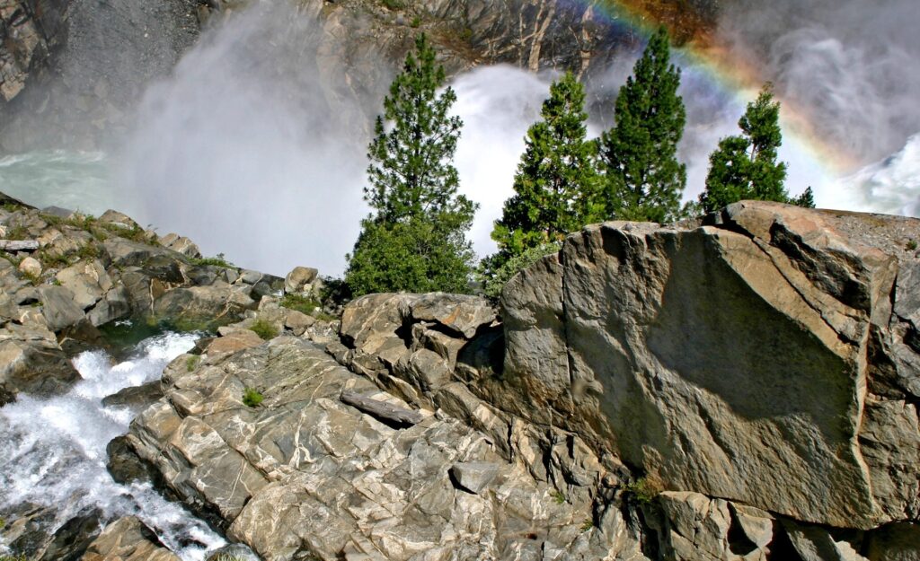 Powerful waterfall with mist and rainbow over rugged stones and green trees natural wallpaper background