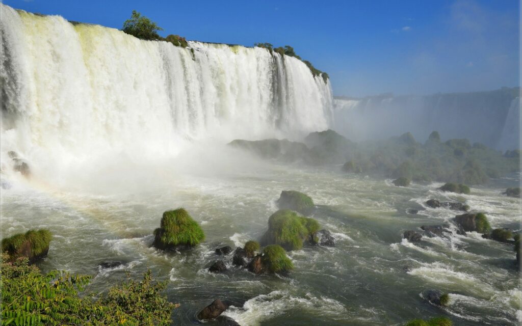 Majestic waterfalls cascading rugged mountains bright blue sky mossy rocks serene landscape wallpaper