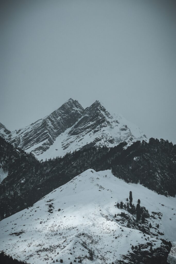Winter mountain landscape with snow-covered peaks and dark tree-lined ridges under overcast sky Wallpaper