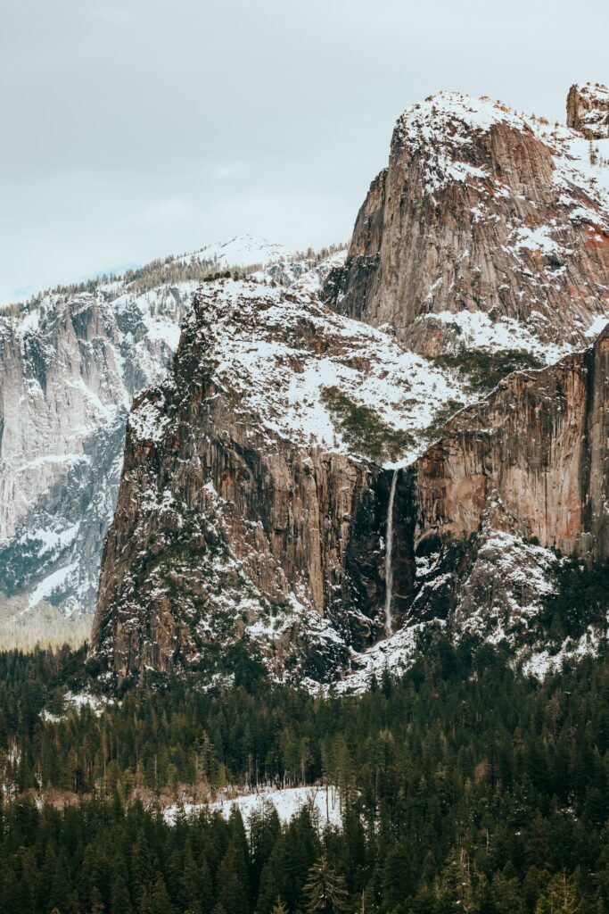 Snowy mountain landscape with rugged rocks and dense evergreen forest in crisp winter scene Wallpaper