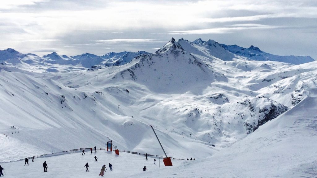 Winter ski slope with adventurous skiers on snow-covered alpine mountains under bright sky Wallpaper