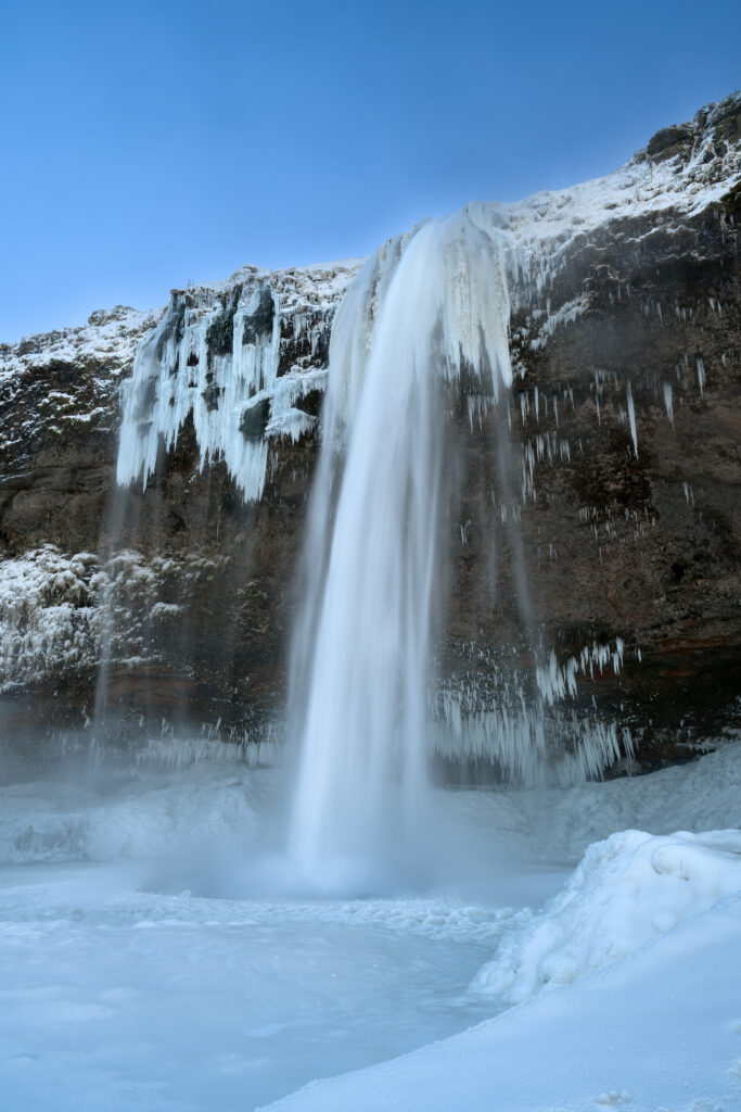 Majestic waterfall cascading icy cliff winter landscape with snow frozen formations clear sky Wallpaper