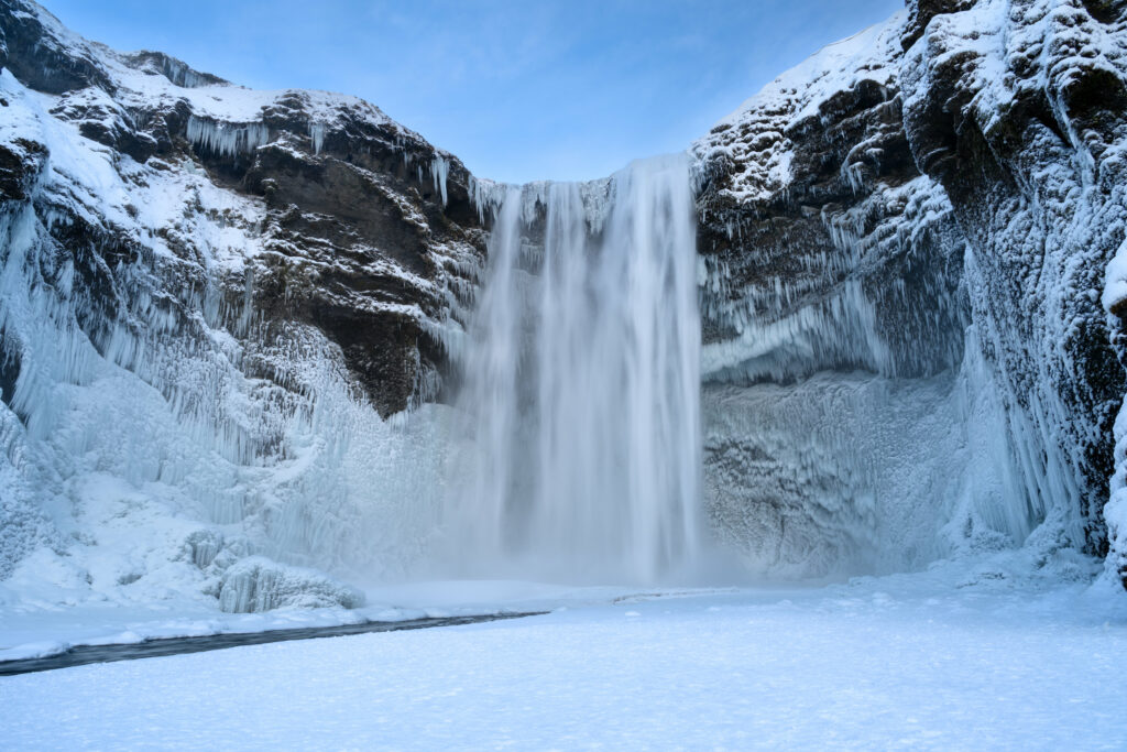 Majestic waterfall cascading over icy rocks in serene winter landscape with snow and blue tones Wallpaper
