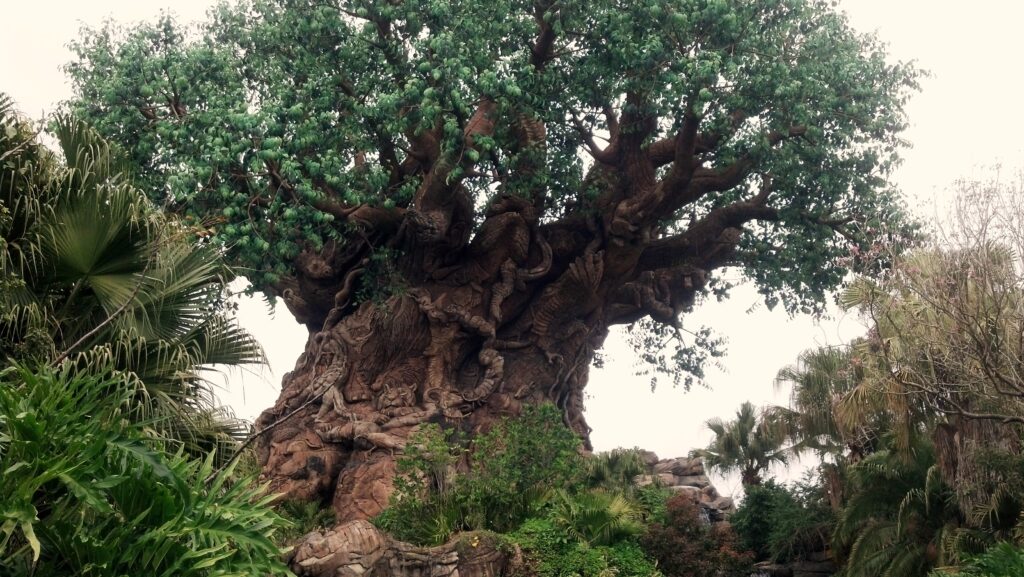 Majestic carved wooden tree with intricate designs surrounded by lush green foliage wallpaper background