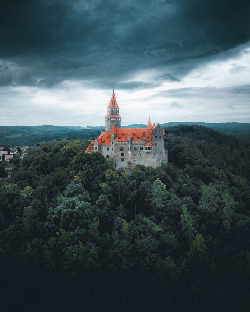 Majestic castle with red rooftops above dense green forest under dramatic moody sky wallpaper background
