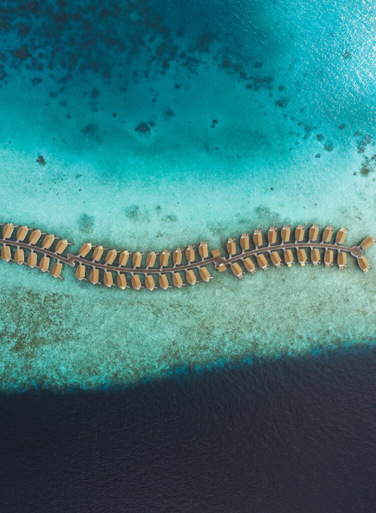 Aerial view of luxurious Maldives bungalows curving over vibrant turquoise lagoon and deep ocean Wallpaper