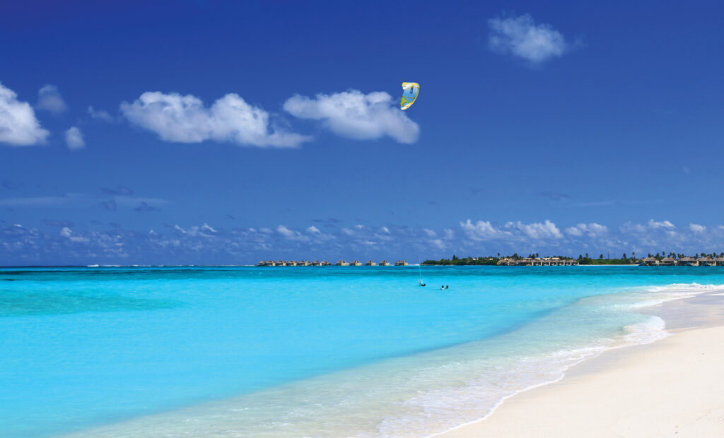 Maldives coastline with turquoise waters white sand and parasail under clear blue sky wallpaper