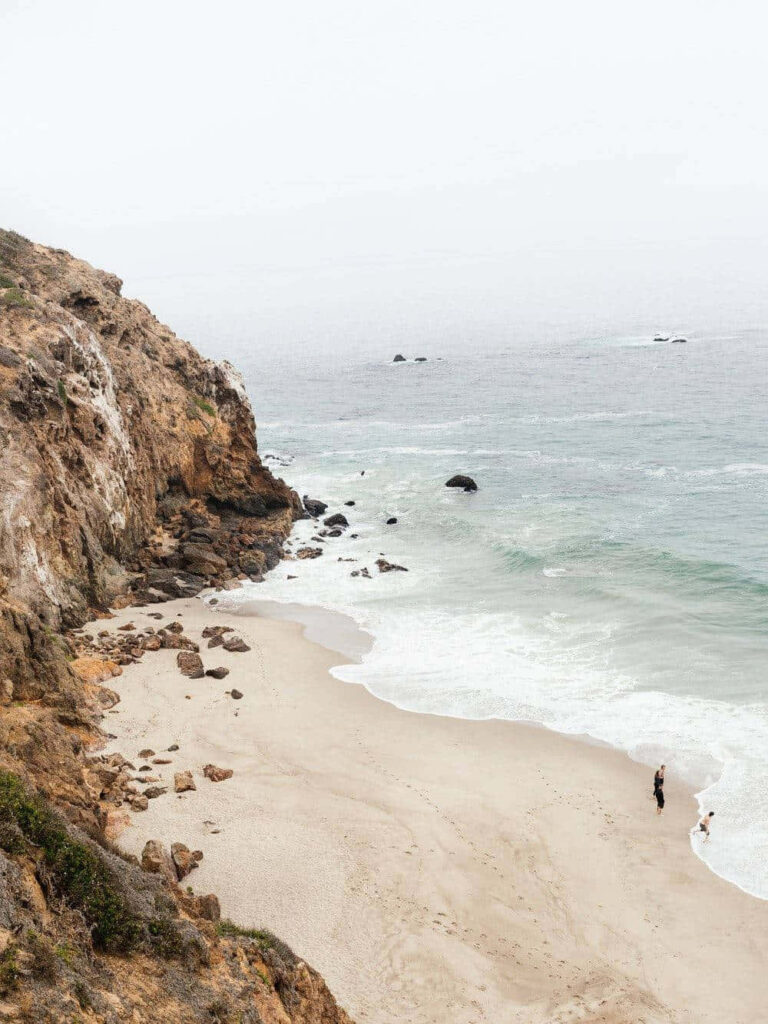 Coastal Bliss: Point Dume's Majestic Promontory and Figures Silhouetted by the Waves Wallpaper