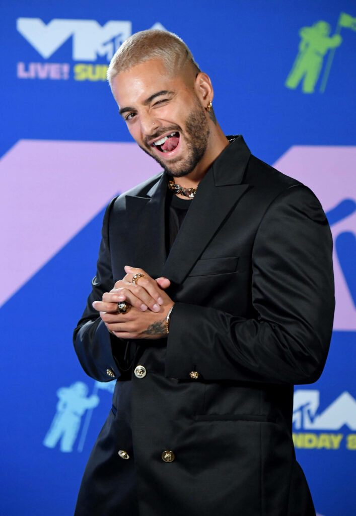 Maluma in black suit with silver wolf fangs exuding charisma and playful rapper energy wallpaper background