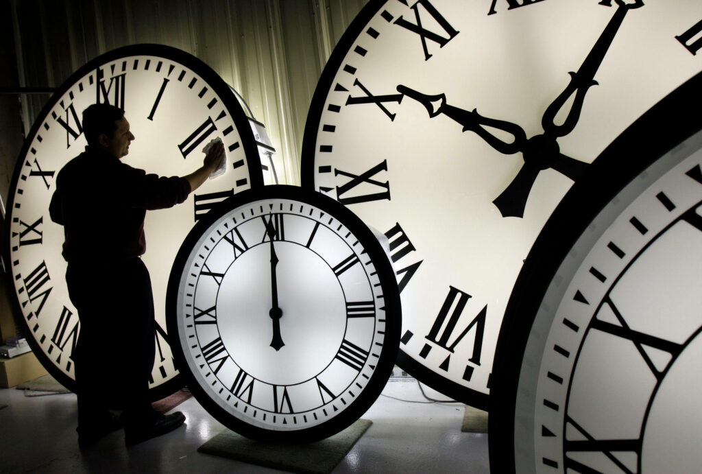 Man cleaning large tower clock face with black Roman numerals in soft white light background Wallpaper