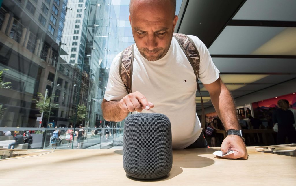 Man examining space gray Apple HomePod smart speaker with textured mesh in bright Apple Store Wallpaper