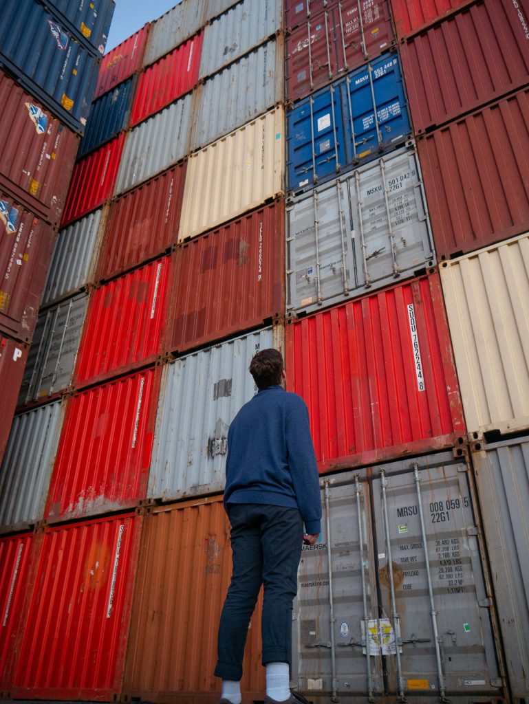 Man looking up at towering colorful stacked shipping containers in vibrant urban industrial scene Wallpaper