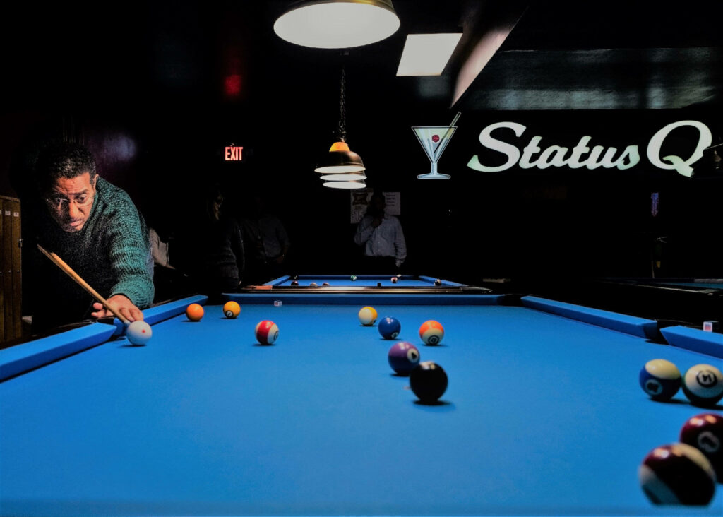 Man aiming pool shot on vibrant blue table in stylish bar with warm lights and glowing sign Wallpaper
