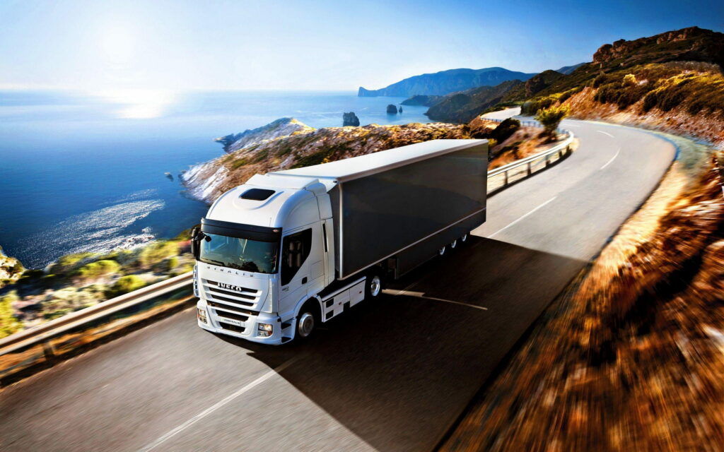 White Iveco Stralis truck driving coastal road bright sunlight ocean backdrop QHD wallpaper