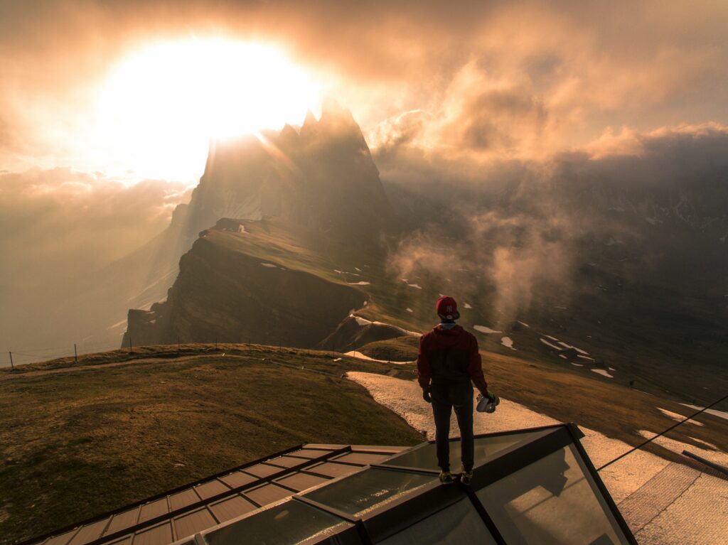 Man standing on glass rooftop with dramatic mountains fog golden sunlight breathtaking view wallpaper