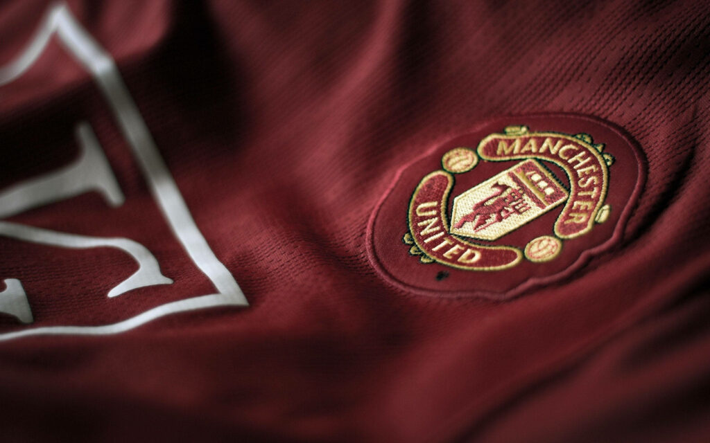 Close-up of Manchester United logo embroidered on rich red fabric wallpaper background