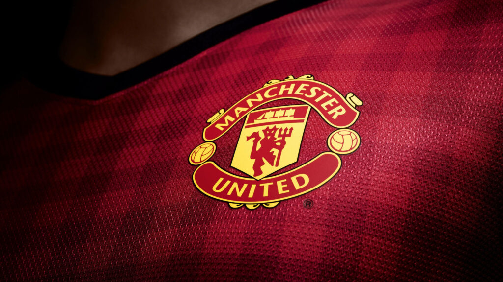 Close-up of Manchester United logo on textured red jersey background football wallpaper