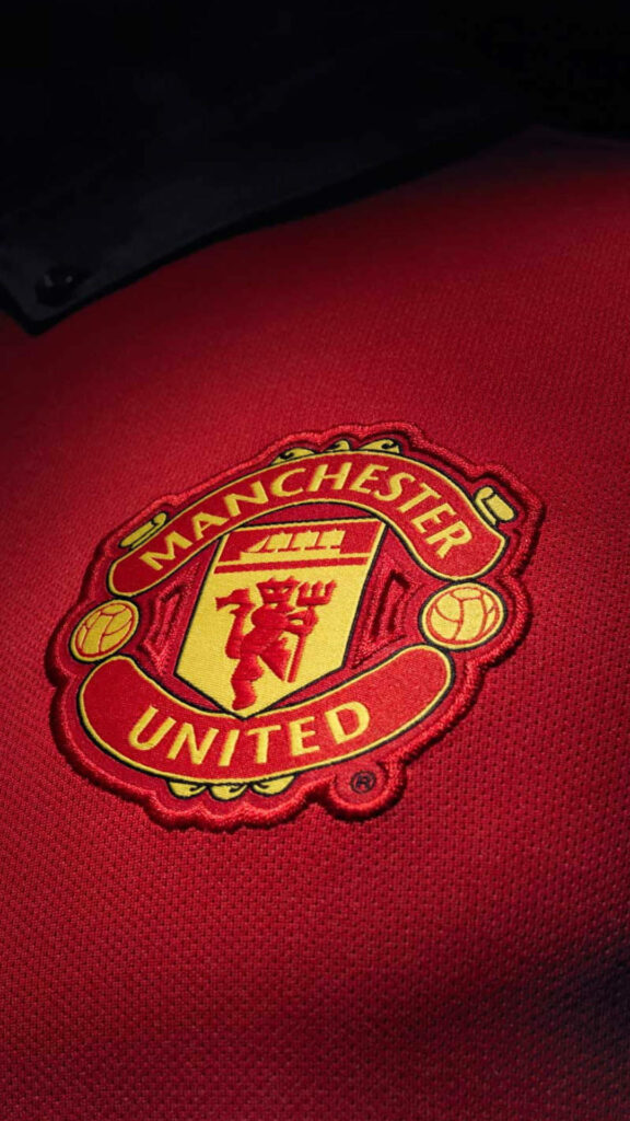 Close-up of Manchester United shirt patch with classic red and gold crest on textured red background Wallpaper