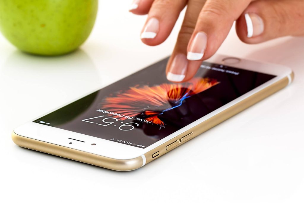 Manicured hand touching gold smartphone screen with vibrant betta fish wallpaper and green apple background