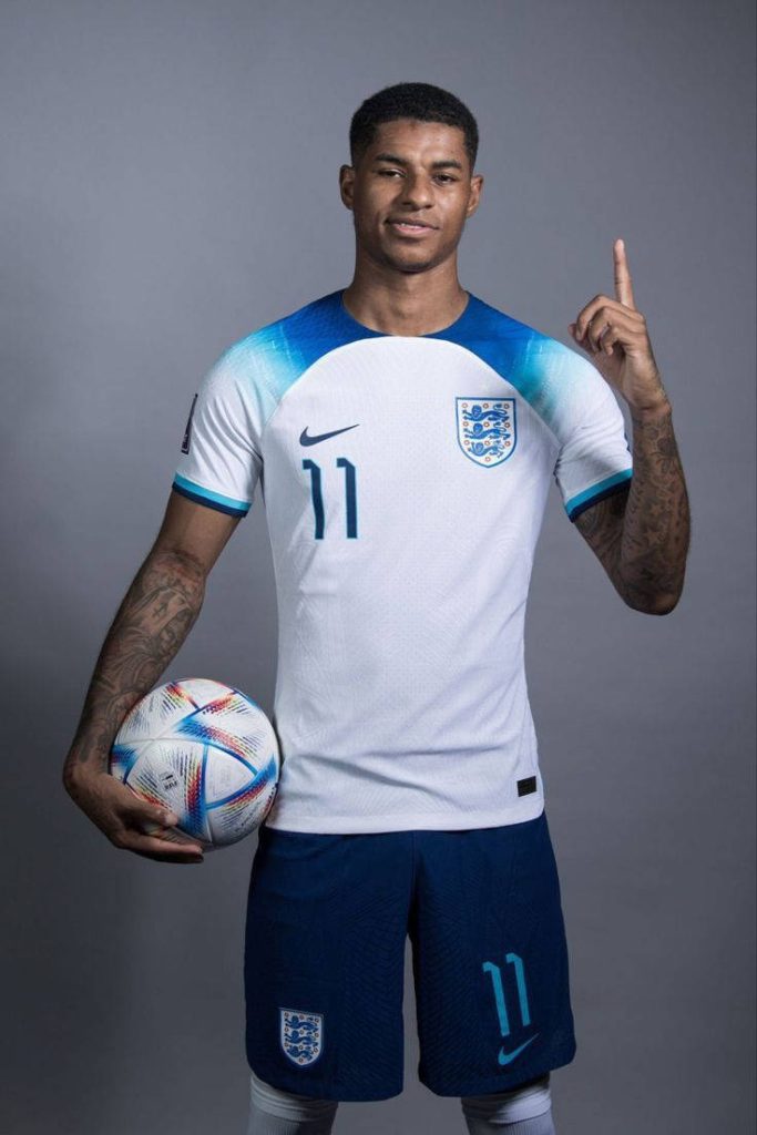 Marcus Rashford England football star in white blue kit holding ball pointing up studio portrait Wallpaper