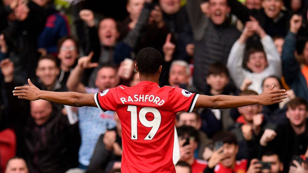 Marcus Rashford celebrating goal in red number 19 jersey with blurred crowd background wallpaper