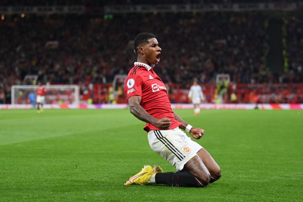 Marcus Rashford celebrating goal kneeling on pitch vibrant Manchester United football wallpaper background